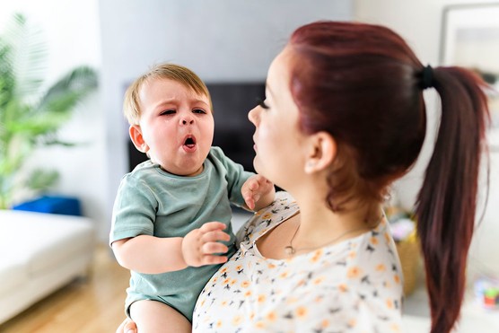 baby coughing in mother's arms at home