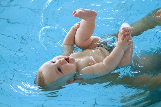 young baby lying on back in water during first swimming lesson