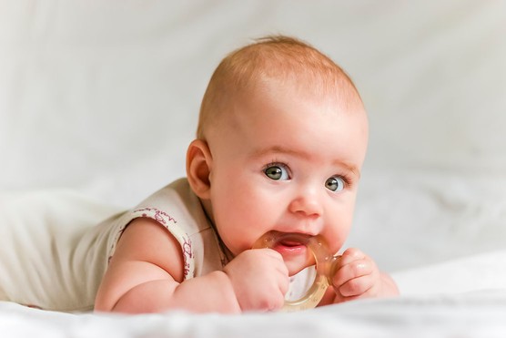 baby girl lying on her front with a teething toy in her mouth