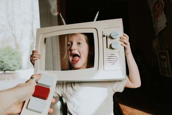 A parent points a simple TV remote at a toy TV, where a little girl looks excited to be the star of her own TV show. Conceptual image depicting attention, play, imagination and parenting noisy children!