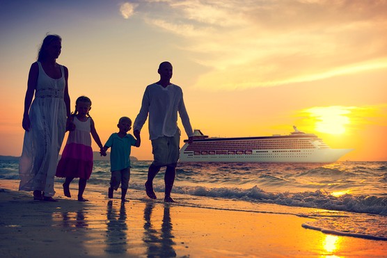 family of four walking along a beach at sunset with a cruise ship in background