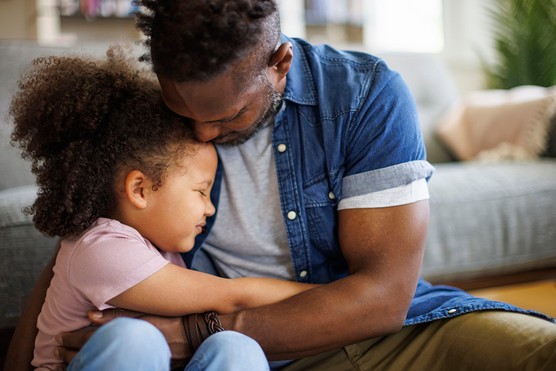 father cuddling young daughter who is sad