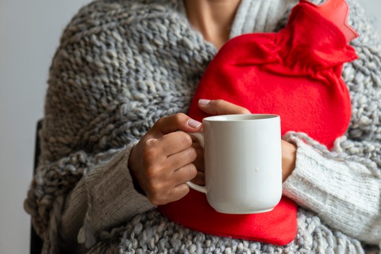 woman holding hot water bottle and a hot drink