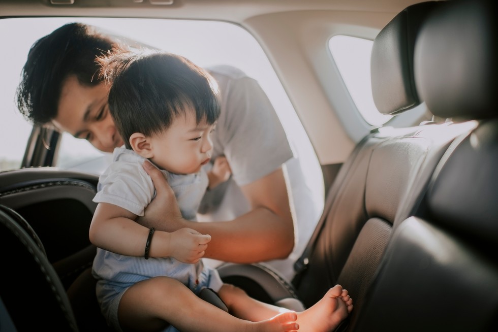 asian chinese father putting his son baby boy sitting in baby seat back seat of car during outing with his parent dad putting child into car seat in a car