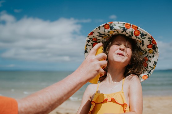 A parent applies sunscreen to a child's face - she braces as she prepares to be spritzed in the face