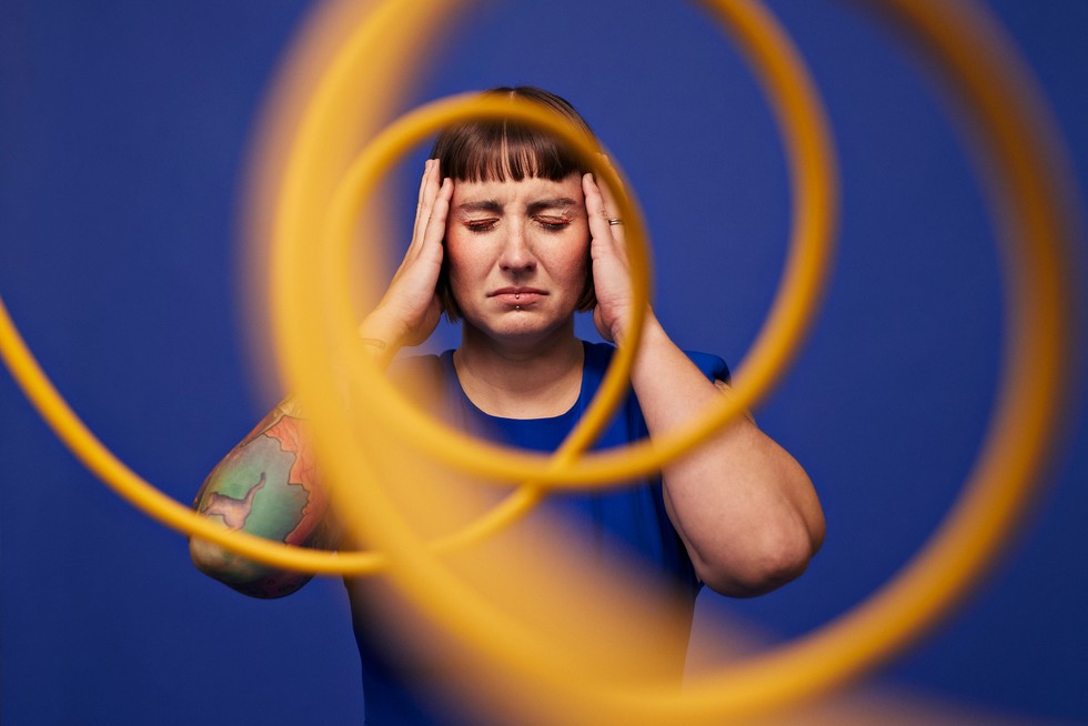 Woman with head in hands behind spiral cables Woman with head in hands standing with eyes closed behind spiral cables against blue background
