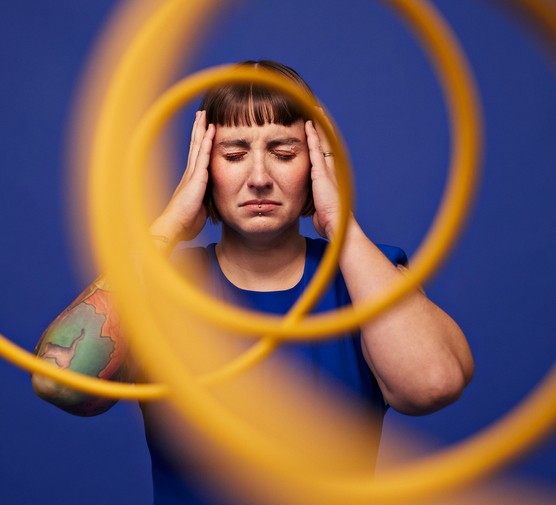 Woman with head in hands behind spiral cables Woman with head in hands standing with eyes closed behind spiral cables against blue background