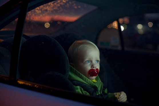 Baby boy (12-18 months) sitting in back seat of car with a dummy in his mouth at night