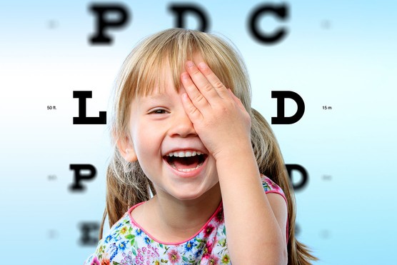 young girl having an eye test looking happy with chart behind her
