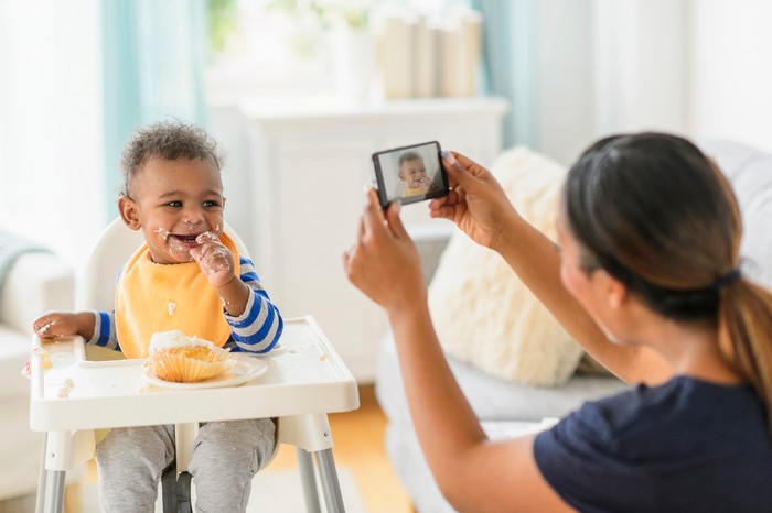 Mixed race mother photographing messy baby boy in high chair Mixed race mother photographing messy baby boy in high chair