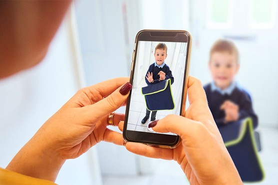 mother's hands taking a picture on her phone of her son in his school uniform on the first day of school