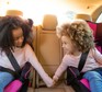 sisters in back of car in car seats, holding hands