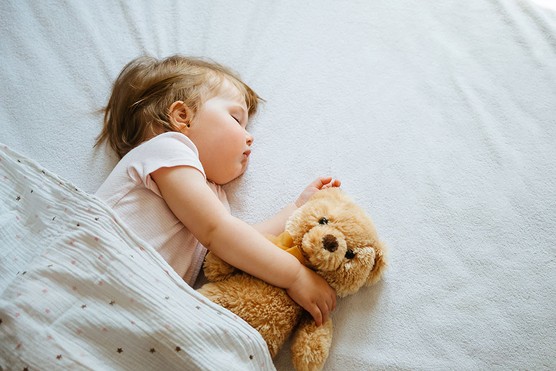 girl toddler asleep in bed with a teddy bear