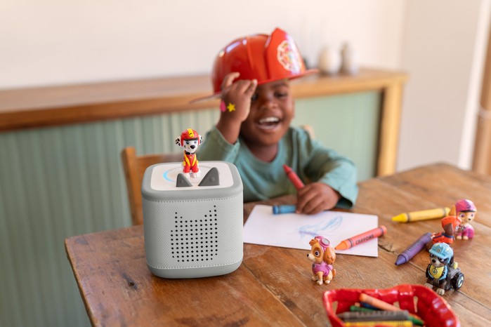 A child wearing a Paw Patrol hat laughing while drawing and listening to Paw Patrol on Toniebox 2